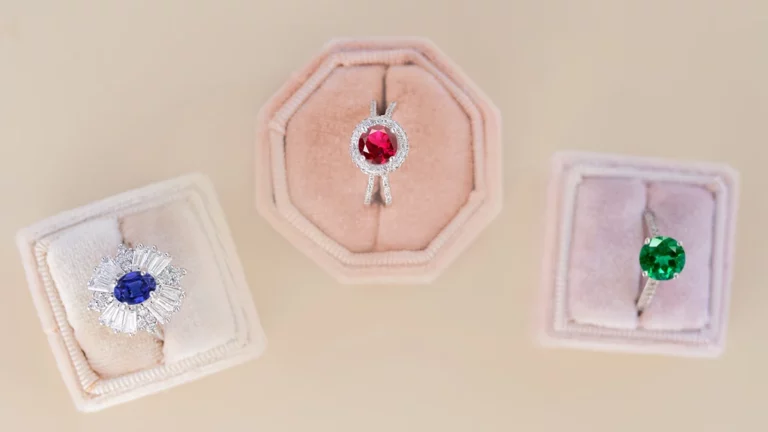 a sapphire ring, an emerald ring, and a ruby ring in separate ring boxes